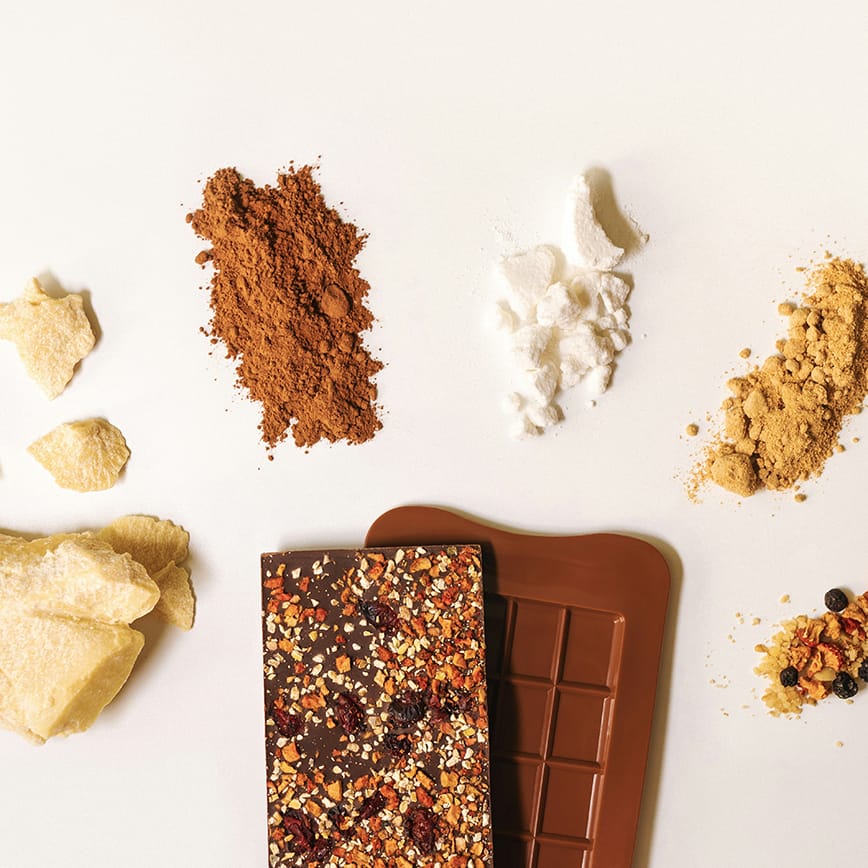 Proteinreiche Schokoladensnacks mit verschiedenen Zutaten und Pulvern auf weißem Hintergrund.
